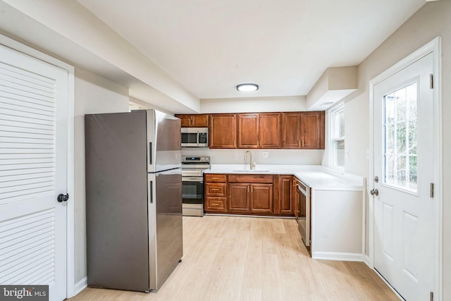 kitchen with stainless steel appliances, a sink, light countertops, light wood finished floors, and brown cabinetry