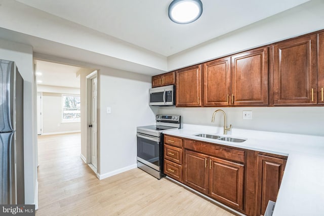 kitchen featuring baseboards, appliances with stainless steel finishes, light countertops, light wood-type flooring, and a sink