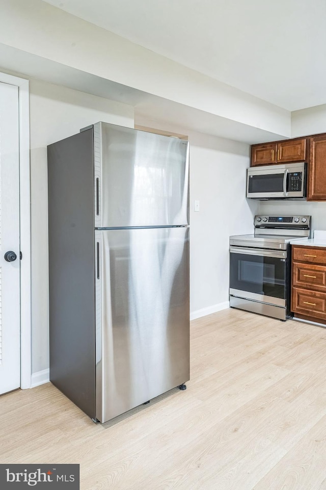 kitchen featuring appliances with stainless steel finishes, light countertops, baseboards, and light wood finished floors