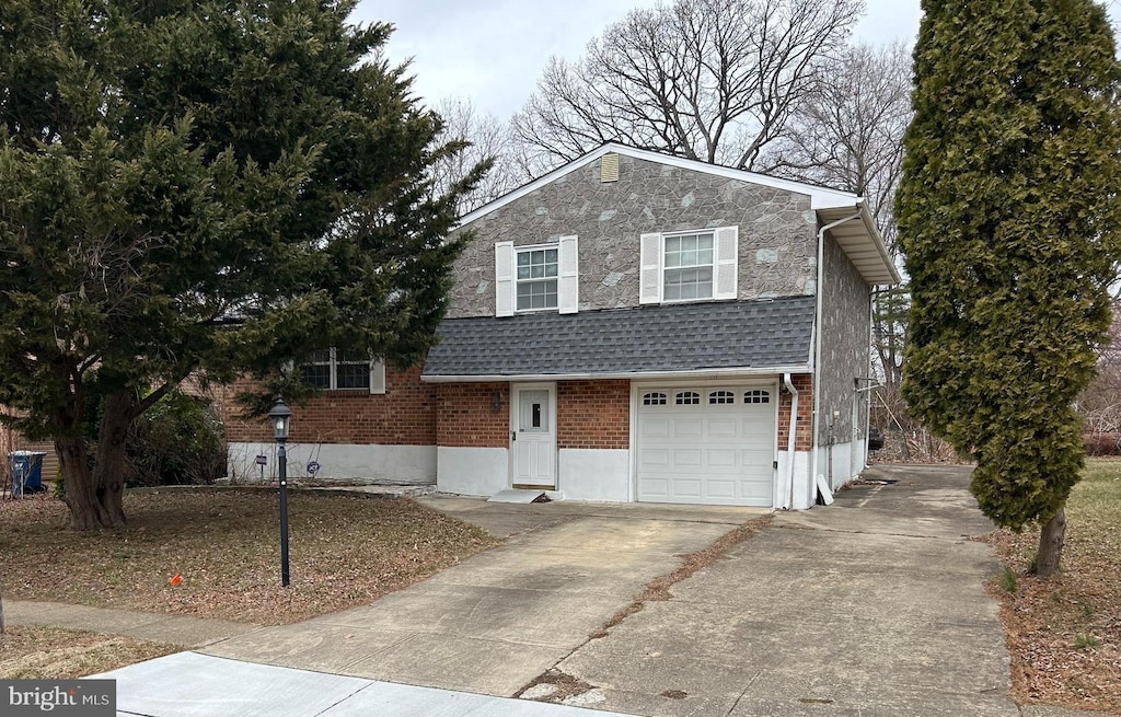 tri-level home with brick siding, a shingled roof, an attached garage, stone siding, and driveway