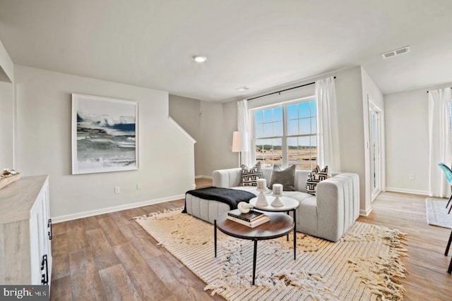 living room featuring visible vents, light wood-style flooring, and baseboards