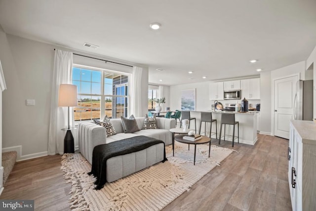 living room featuring light wood-style flooring, visible vents, baseboards, and recessed lighting