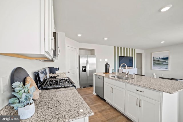 kitchen featuring light wood-style flooring, a kitchen island with sink, stainless steel appliances, a sink, and white cabinets