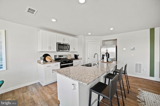 kitchen with stainless steel appliances, visible vents, a sink, and light stone countertops