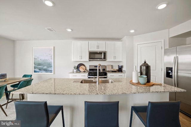 kitchen with a kitchen bar, appliances with stainless steel finishes, white cabinets, and recessed lighting