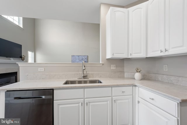 kitchen featuring a sink, white cabinets, dishwasher, and a glass covered fireplace