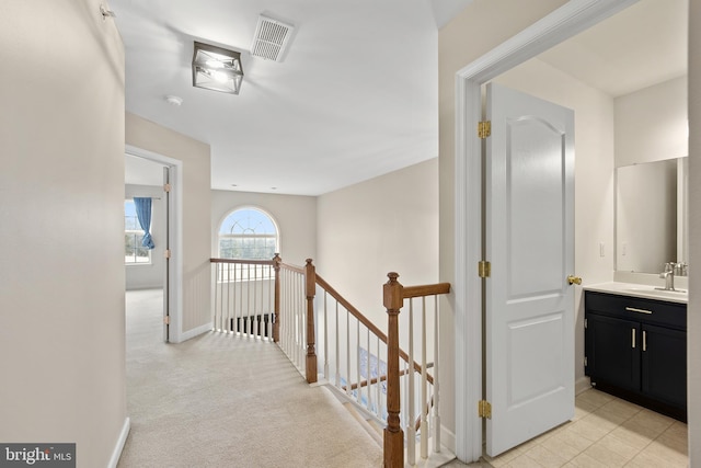 hallway featuring baseboards, visible vents, light colored carpet, an upstairs landing, and a sink