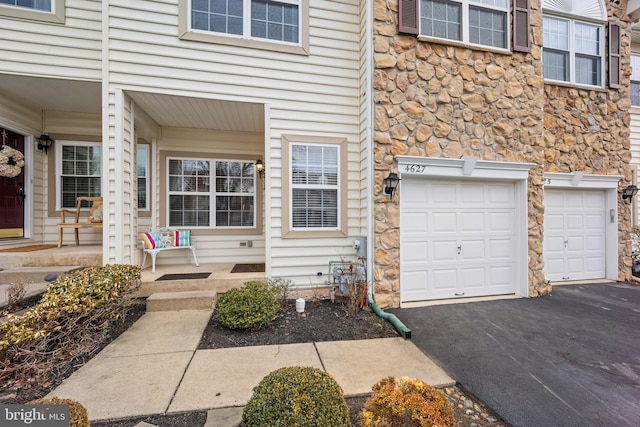 view of exterior entry featuring covered porch, stone siding, driveway, and a garage