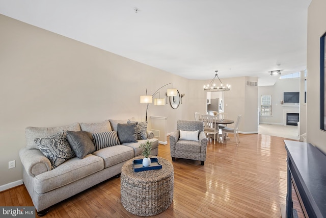 living room featuring light wood-type flooring, visible vents, a glass covered fireplace, and baseboards