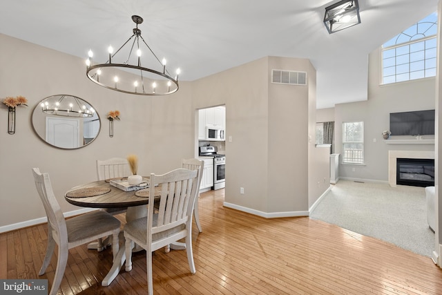 dining room featuring light wood-style flooring, a glass covered fireplace, visible vents, and baseboards