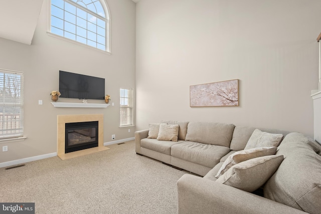 living room featuring carpet, visible vents, a high ceiling, a fireplace with flush hearth, and baseboards