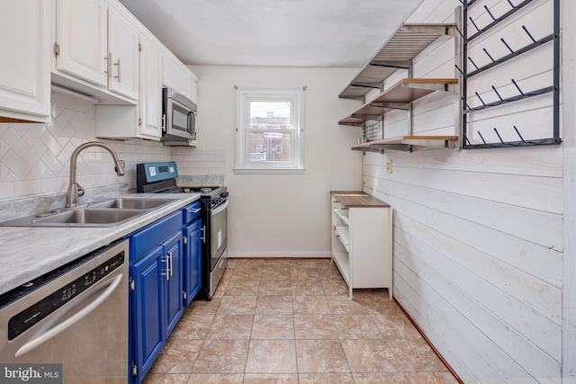 kitchen featuring stainless steel appliances, a sink, white cabinetry, blue cabinetry, and open shelves