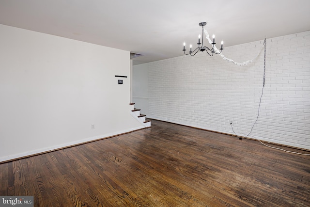 unfurnished dining area featuring a notable chandelier, brick wall, stairway, and wood finished floors