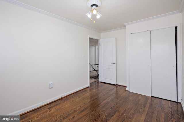 unfurnished bedroom with a closet, dark wood-style flooring, crown molding, and baseboards