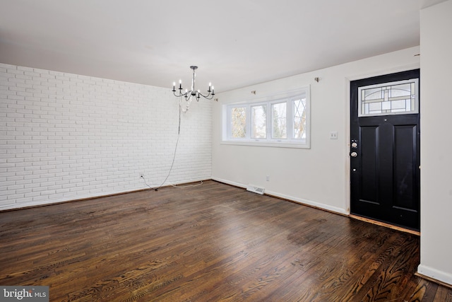 entryway featuring dark wood-type flooring, visible vents, a notable chandelier, and brick wall