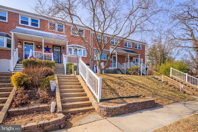 multi unit property with covered porch, stairway, and brick siding