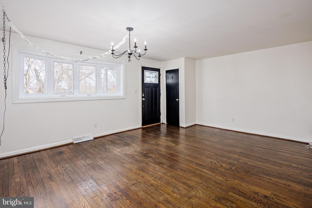 unfurnished dining area with visible vents, dark wood finished floors, a notable chandelier, and baseboards