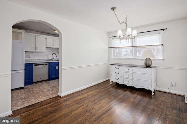 dining space featuring arched walkways, an inviting chandelier, hardwood / wood-style flooring, and baseboards