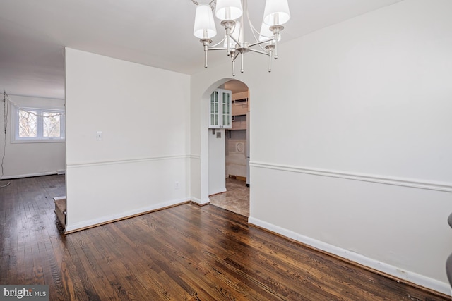 unfurnished dining area with a chandelier, arched walkways, wood-type flooring, and baseboards