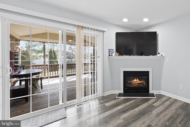 unfurnished living room with a glass covered fireplace, wood finished floors, visible vents, and baseboards