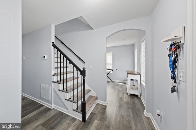 foyer featuring baseboards, visible vents, arched walkways, stairway, and wood finished floors