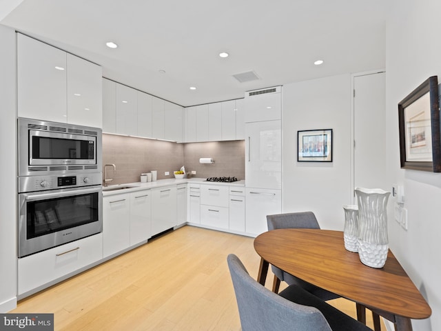 kitchen featuring white cabinets, modern cabinets, stainless steel appliances, light wood-style floors, and a sink