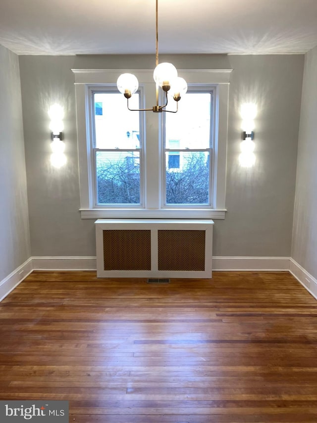 unfurnished dining area featuring a chandelier, baseboards, radiator heating unit, and wood finished floors