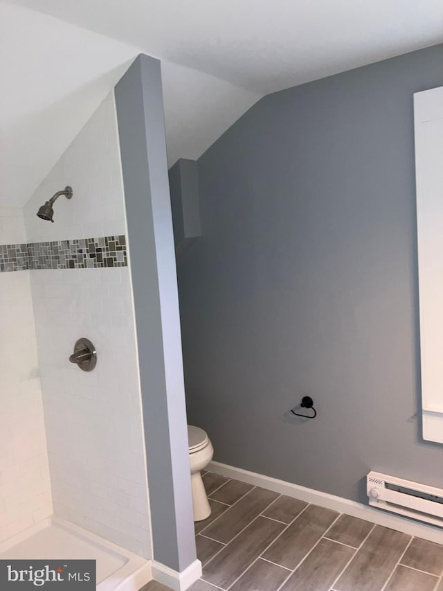 bathroom featuring toilet, a baseboard heating unit, baseboards, vaulted ceiling, and tiled shower