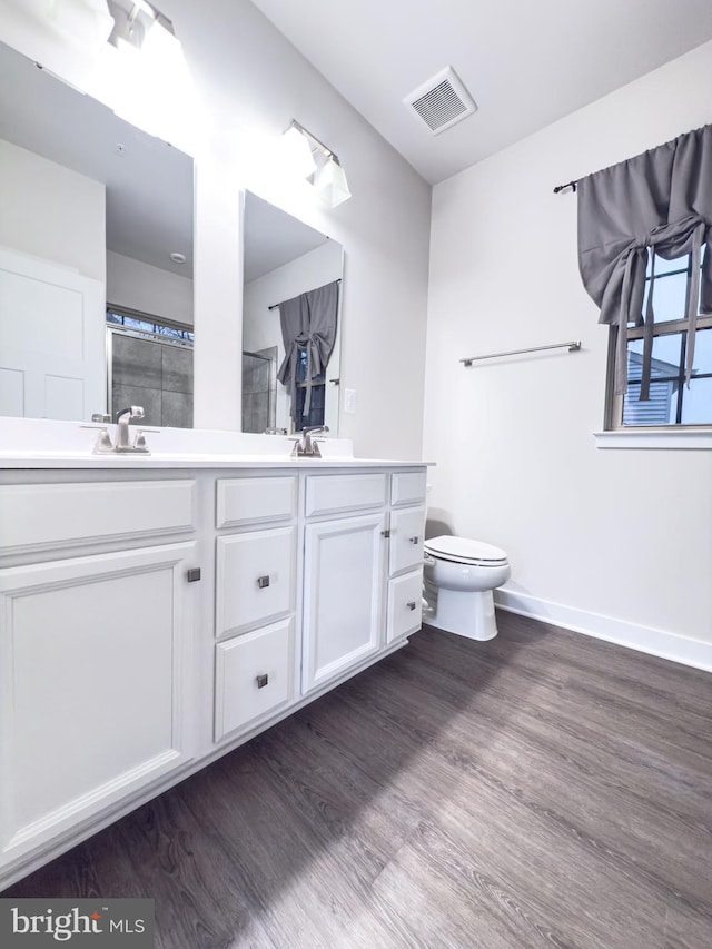 full bath featuring double vanity, visible vents, toilet, and wood finished floors