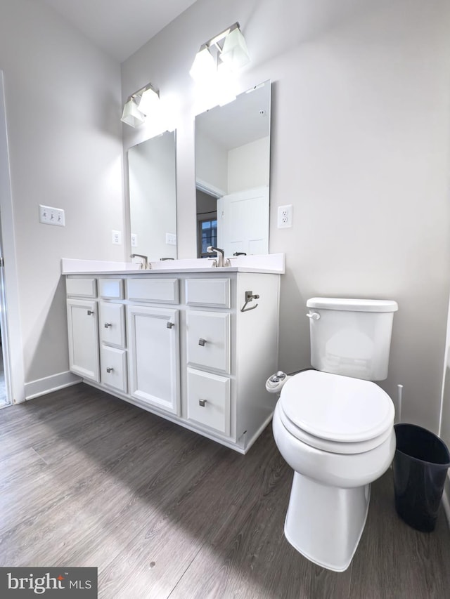 bathroom featuring toilet, baseboards, wood finished floors, and vanity