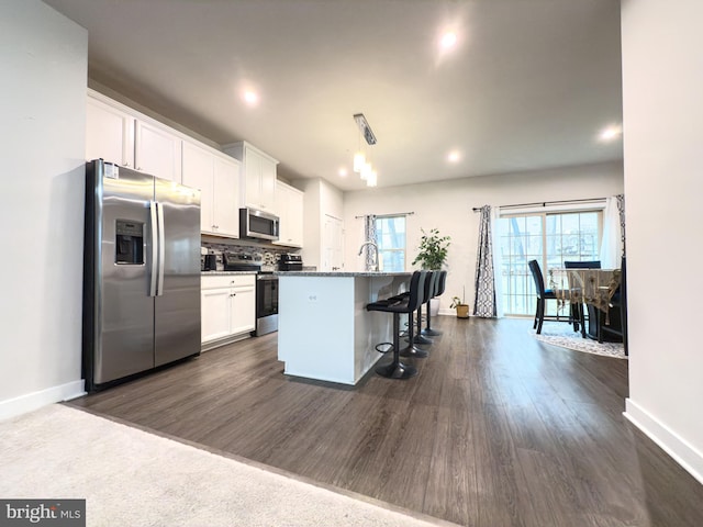 kitchen with stainless steel appliances, white cabinetry, backsplash, an island with sink, and a kitchen bar