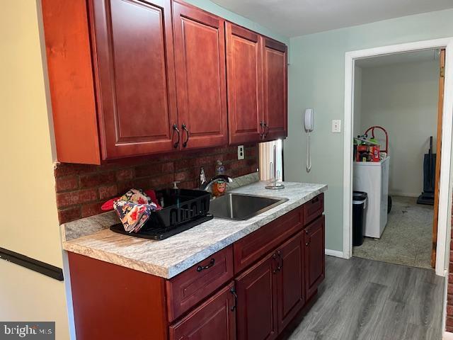 kitchen with dark wood-style flooring, a sink, light countertops, tasteful backsplash, and washer / dryer