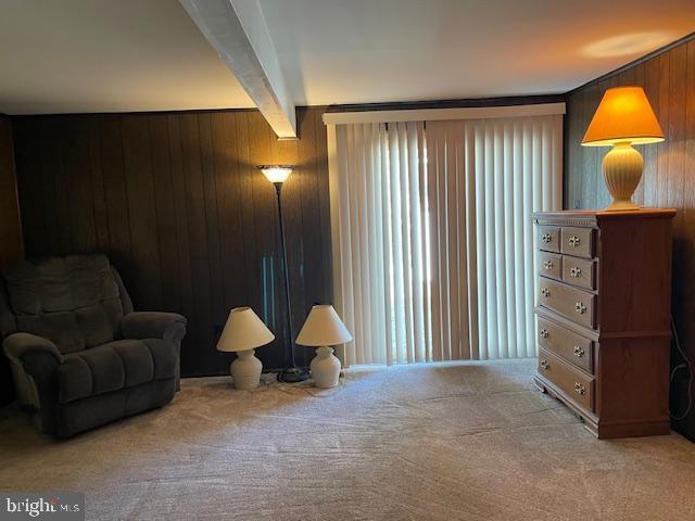 living area featuring wooden walls, beamed ceiling, and carpet flooring