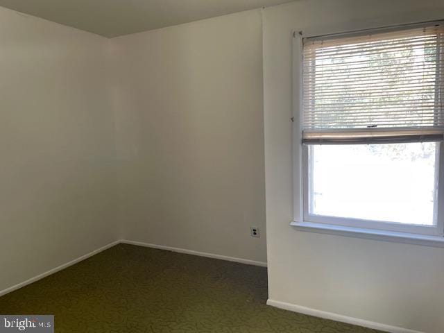 unfurnished room featuring dark carpet and baseboards