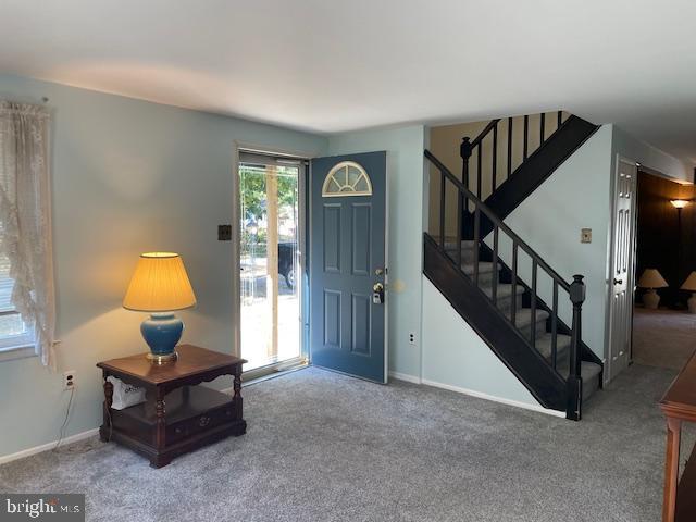 foyer entrance with stairs, baseboards, and carpet flooring