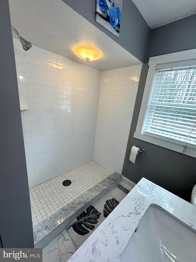 full bathroom with marble finish floor, a tile shower, and a textured ceiling