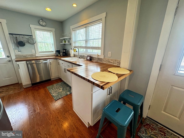 kitchen featuring dark wood-type flooring, a sink, wood counters, dishwasher, and a peninsula