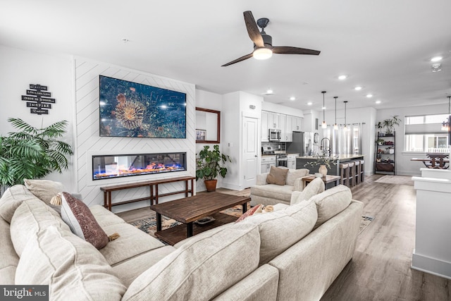 living room featuring recessed lighting, light wood-style flooring, a large fireplace, ceiling fan, and baseboards