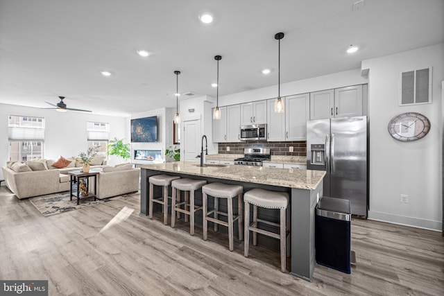 kitchen with a center island with sink, visible vents, appliances with stainless steel finishes, a kitchen breakfast bar, and wood finished floors