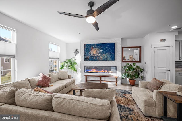 living room with a large fireplace, ceiling fan, and wood finished floors