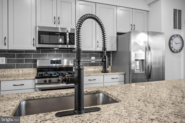 kitchen with stainless steel appliances, visible vents, decorative backsplash, and light stone countertops