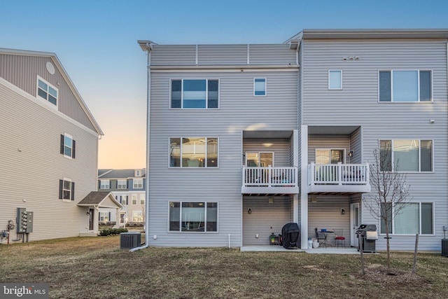 back of house featuring cooling unit, a patio, a balcony, and a lawn