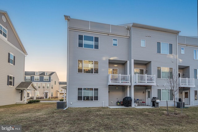 back of property at dusk with a patio area, a yard, and central air condition unit