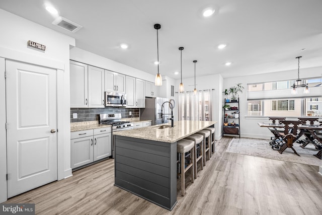 kitchen featuring stainless steel appliances, tasteful backsplash, visible vents, light wood-style flooring, and a sink