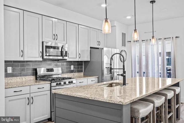 kitchen featuring tasteful backsplash, light stone counters, a kitchen island with sink, stainless steel appliances, and a sink