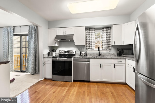 kitchen with plenty of natural light, appliances with stainless steel finishes, under cabinet range hood, white cabinetry, and a sink