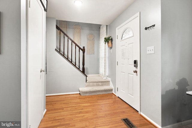 foyer with stairs, wood finished floors, visible vents, and baseboards