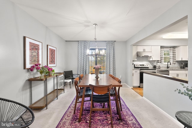 dining room featuring a chandelier, light colored carpet, plenty of natural light, and baseboards