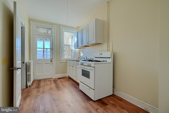 611 E 37th St, Baltimore, MD 21218 - kitchen featuring white range with gas stovetop, wood finished floors, baseboards, backsplash, and radiator