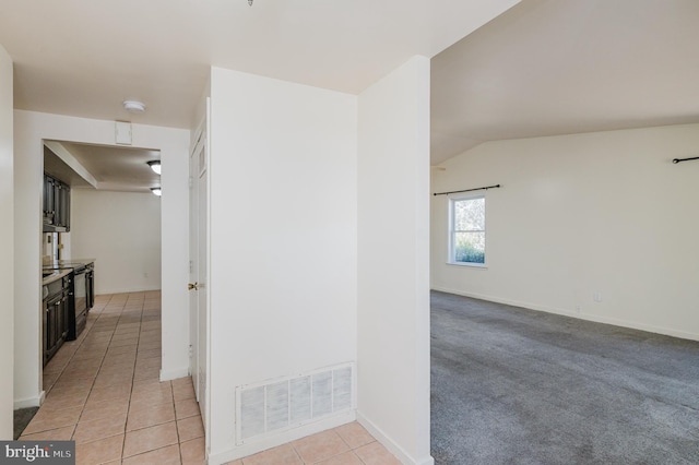 hall featuring light tile patterned floors, visible vents, baseboards, and vaulted ceiling